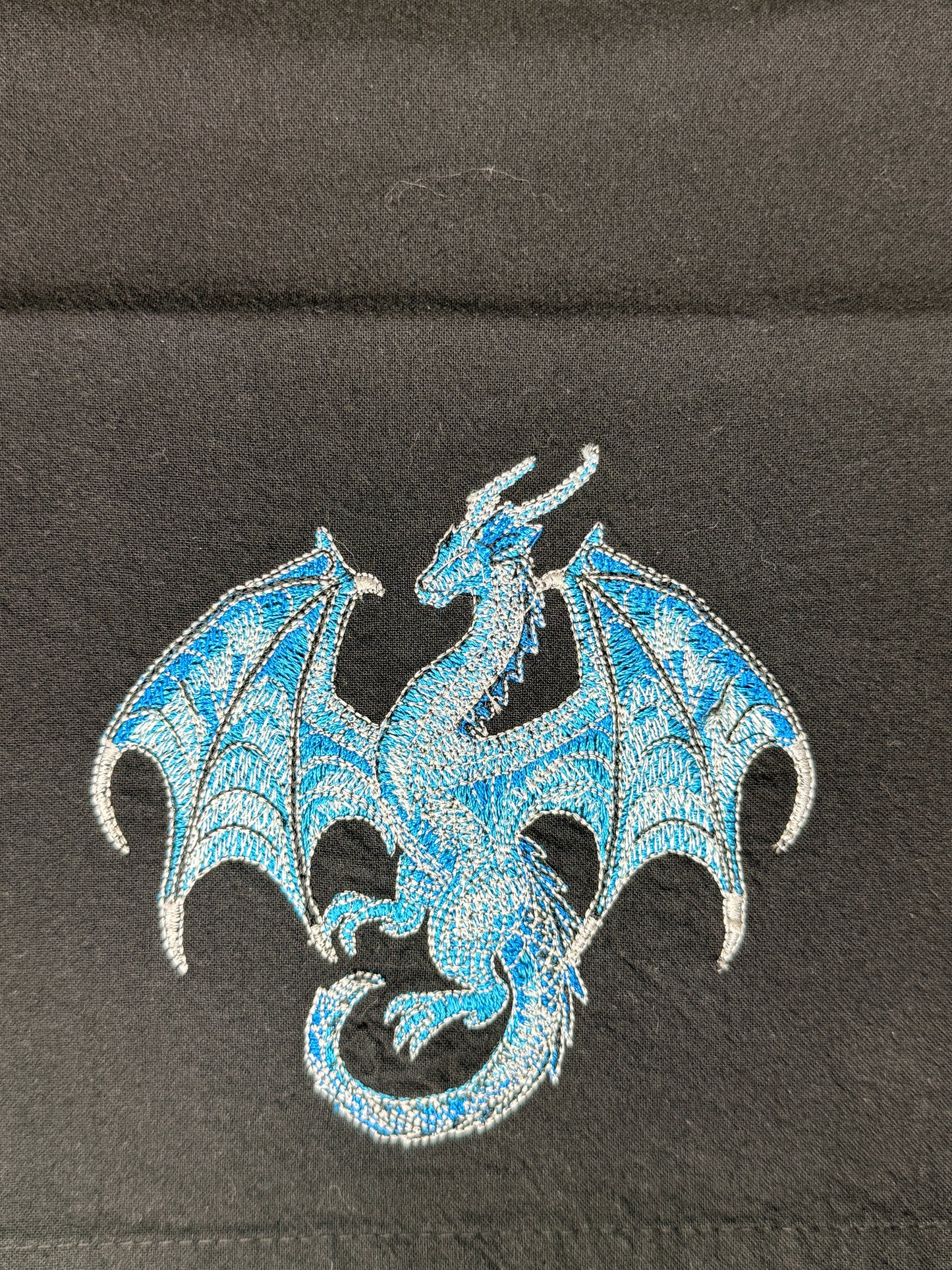 A blue and silver embroidered dragon patch on a black fabric background.