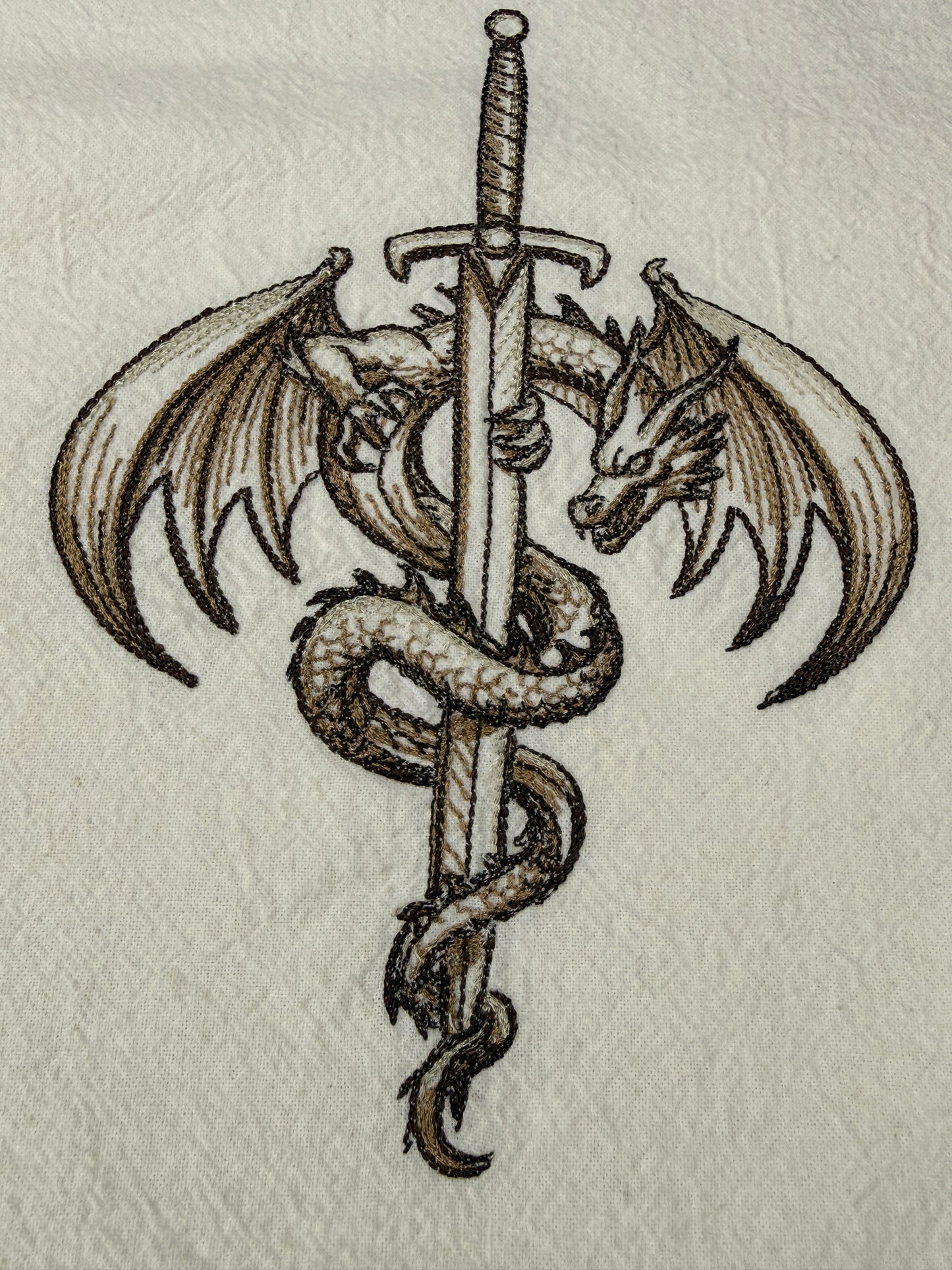 A detailed embroidery design of a winged dragon wrapped around a vertical sword, shown on a textured off-white fabric background.