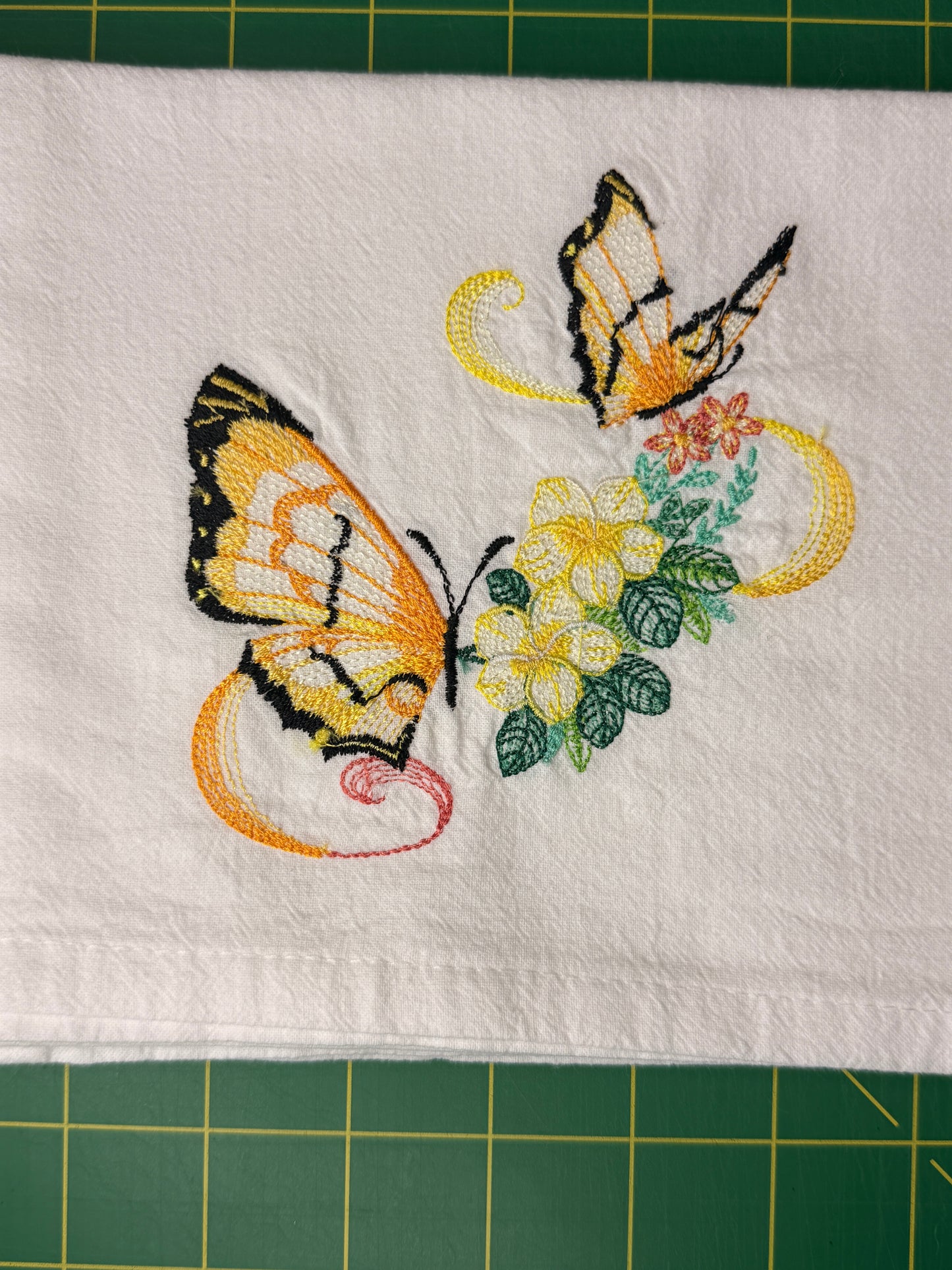 A white fabric towel featuring embroidered butterflies and flowers.