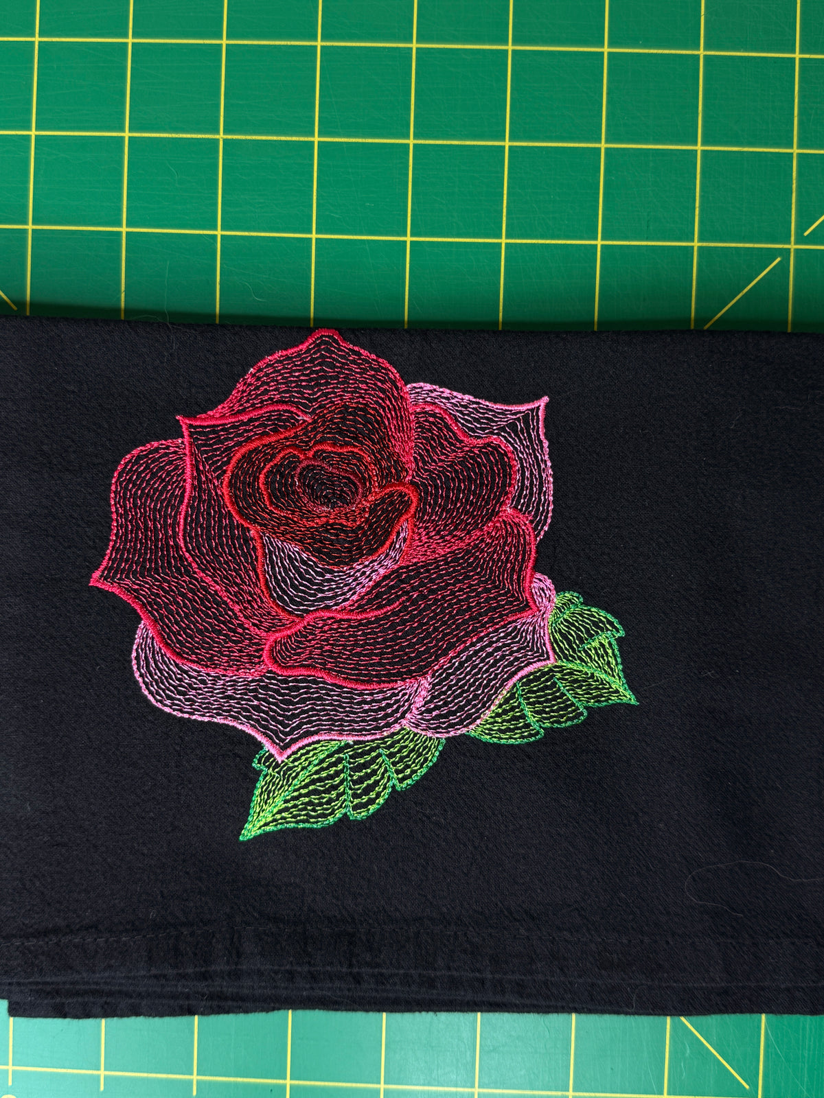 A close-up of a black fabric towel featuring a large embroidered rose design in pink, red, and green.